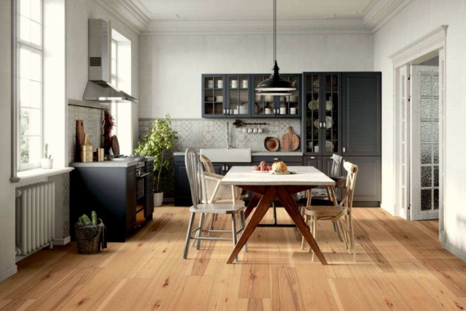 warm toned hardwood flooring in kitchen with dining table and black cabinets.